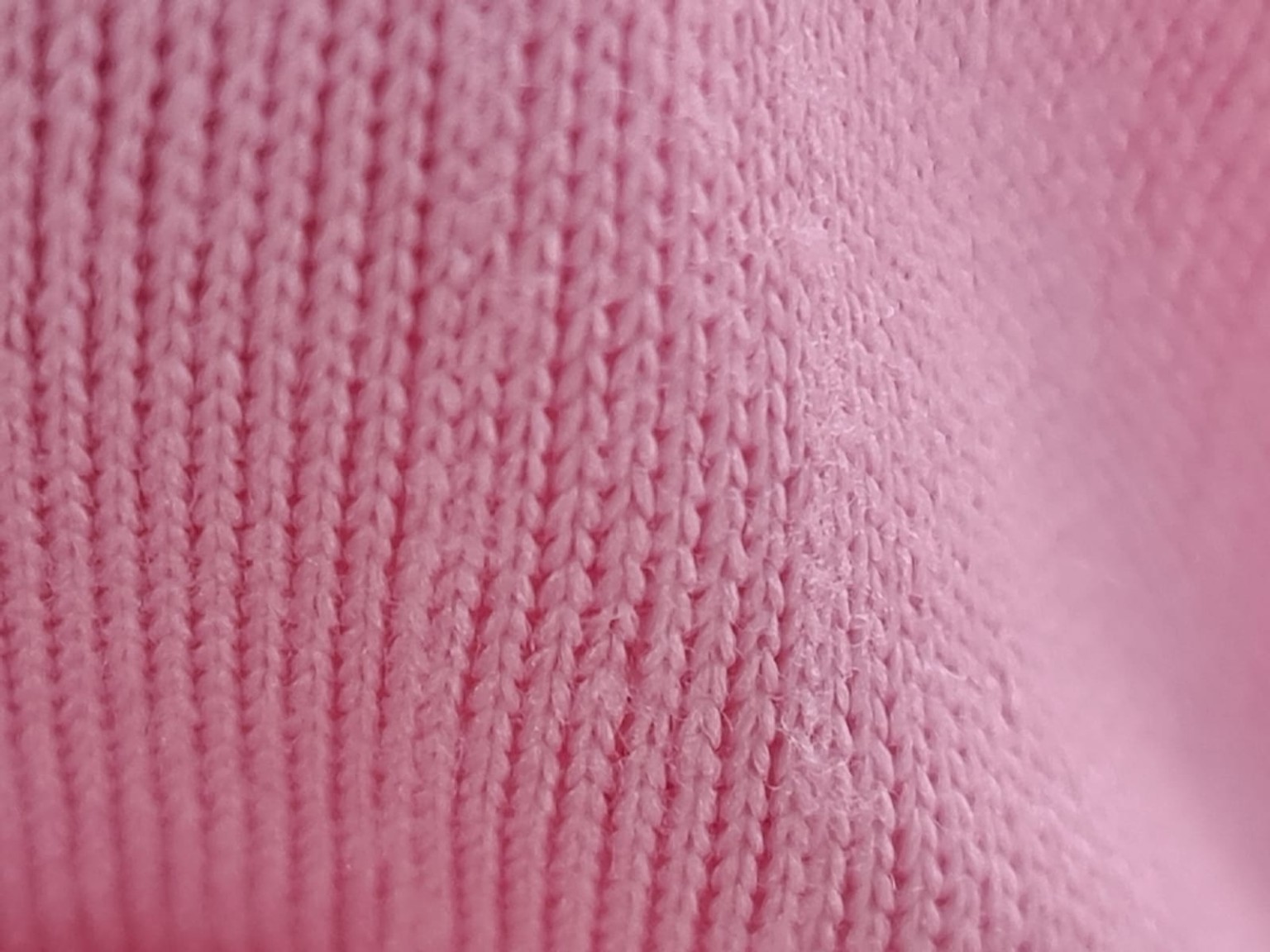 Close de uma malha rosa, mostrando a superfície e a construção em laçadas.